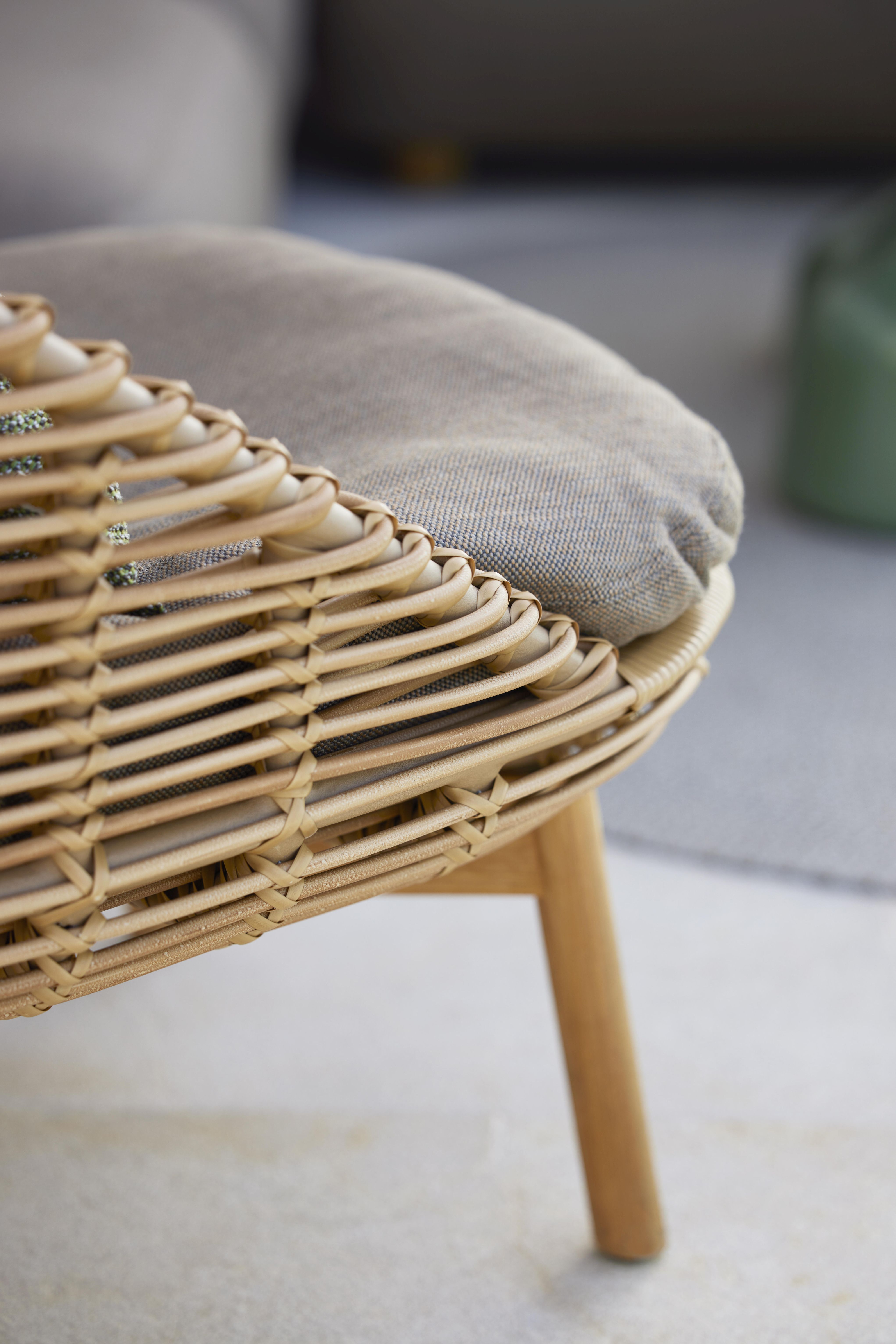 Detailaufnahme: Cane-Line Hive Sessel mit Teakholzbeinen und beigem Sitzkissen aus Rattan.