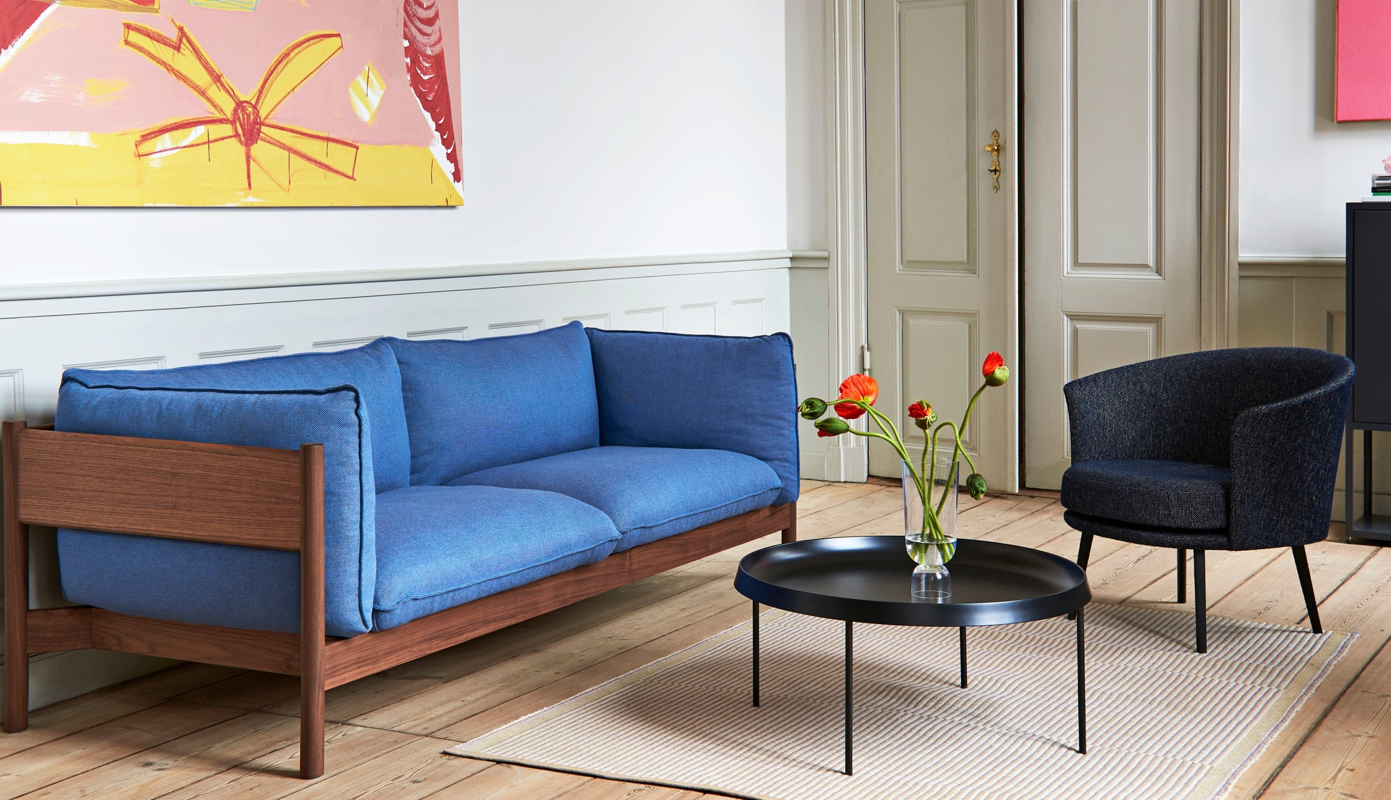 Wohnzimmer mit blauem Sofa, Sessel und schwarzem Couchtisch auf einem Tapis Teppich von Hay.