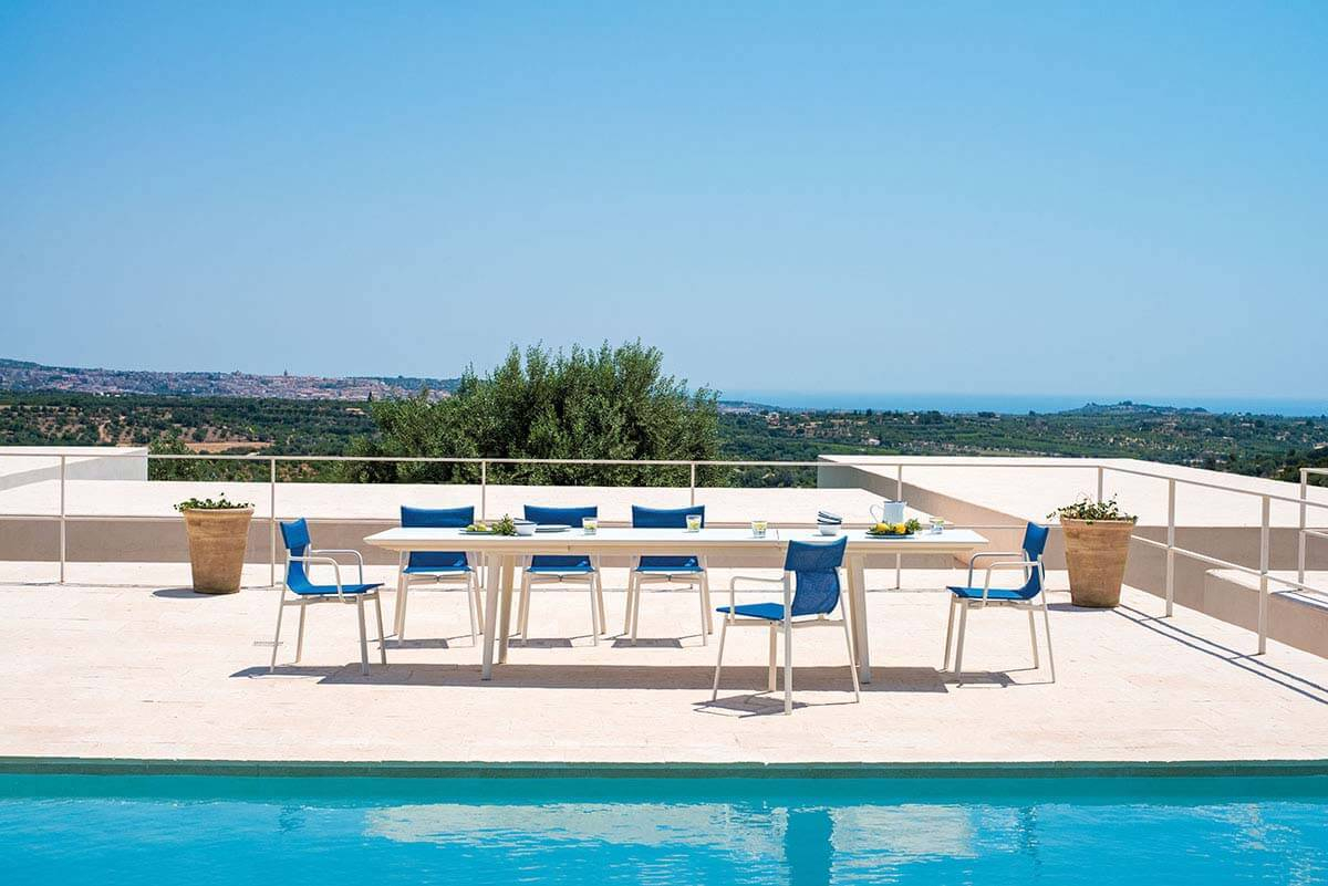 Plus4 Emu Ausziehtisch in Graugrün mit blauen Stühlen am Pool für entspannte Outdoor-Momente.