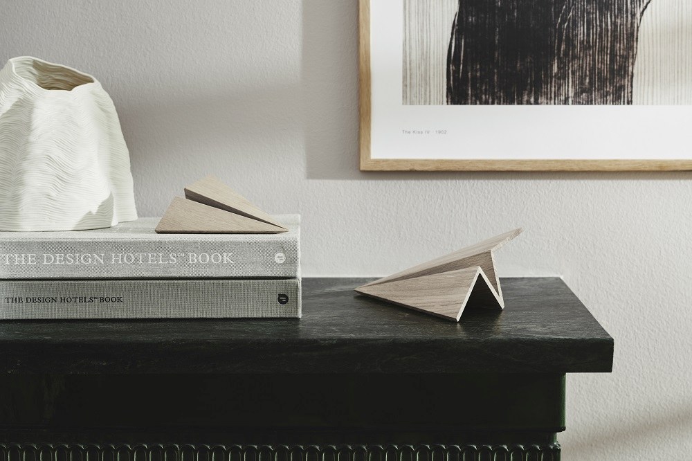 Maverick Paperplane Holzfigur: Geräuchertes Eichenholz Papierflugzeug als Deko-Objekt auf einem Tisch.