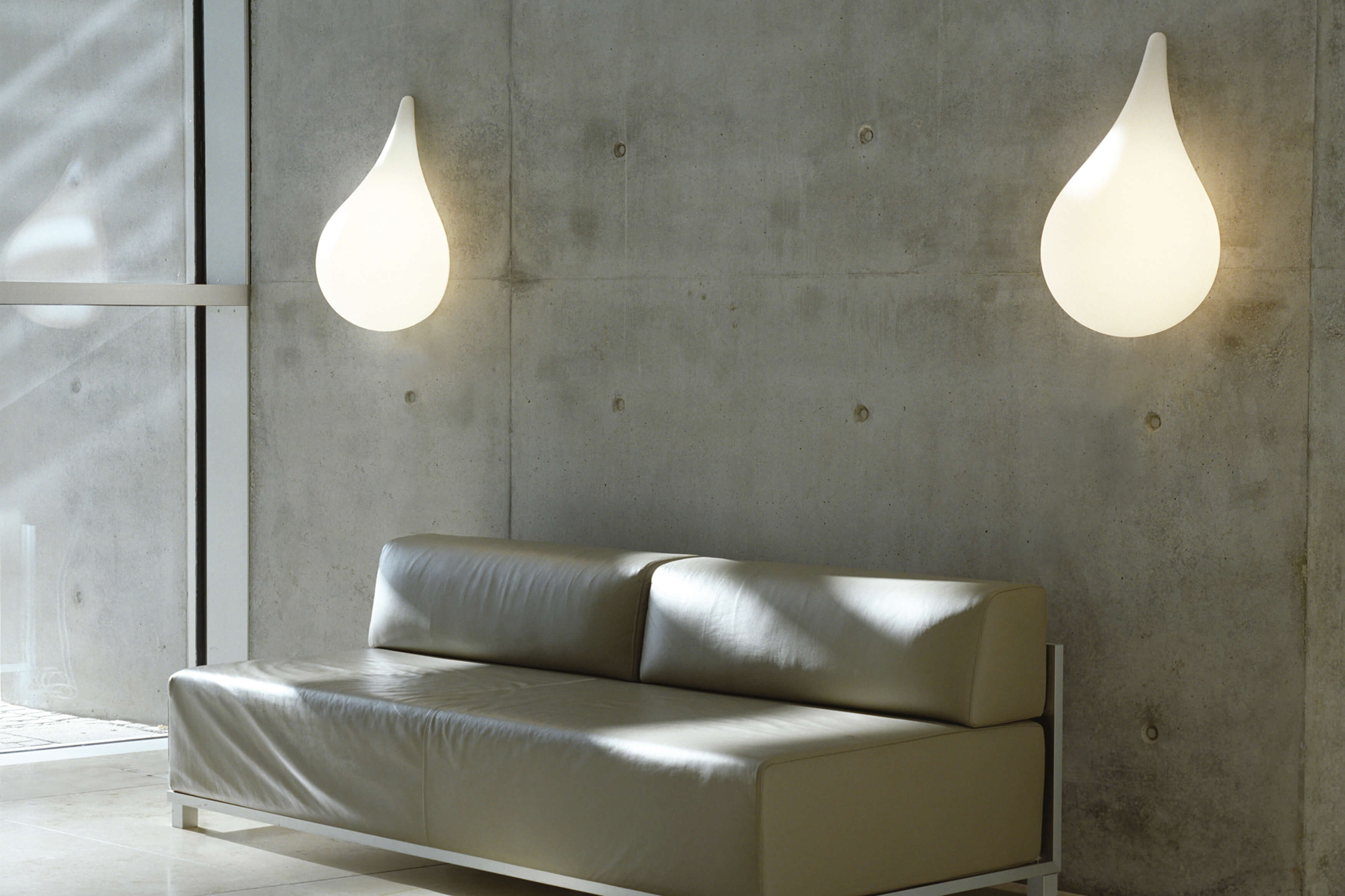 Zwei Liquid Light Drop Wandleuchten von Next an einer Betonwand über einem Sofa.