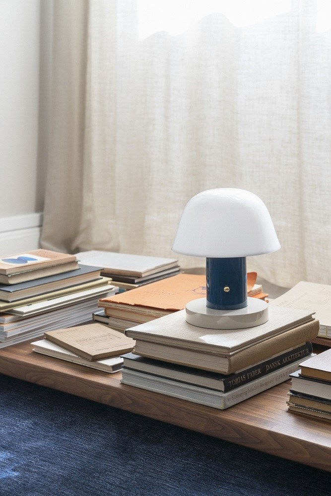 Setago Akkuleuchte Twilight & Sand von AndTradition auf Bücherstapel, stimmungsvolle Tischleuchte.