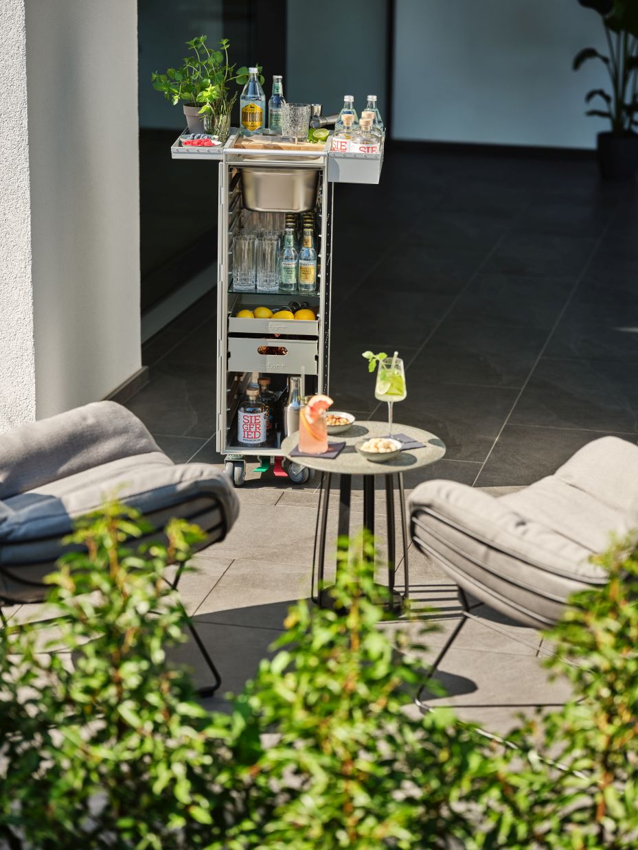 Rivet Rocker Flugzeugtrolley Bordbar mit Getränken und Gläsern auf einer Terrasse. Mobiler Servierwagen für Cocktails.