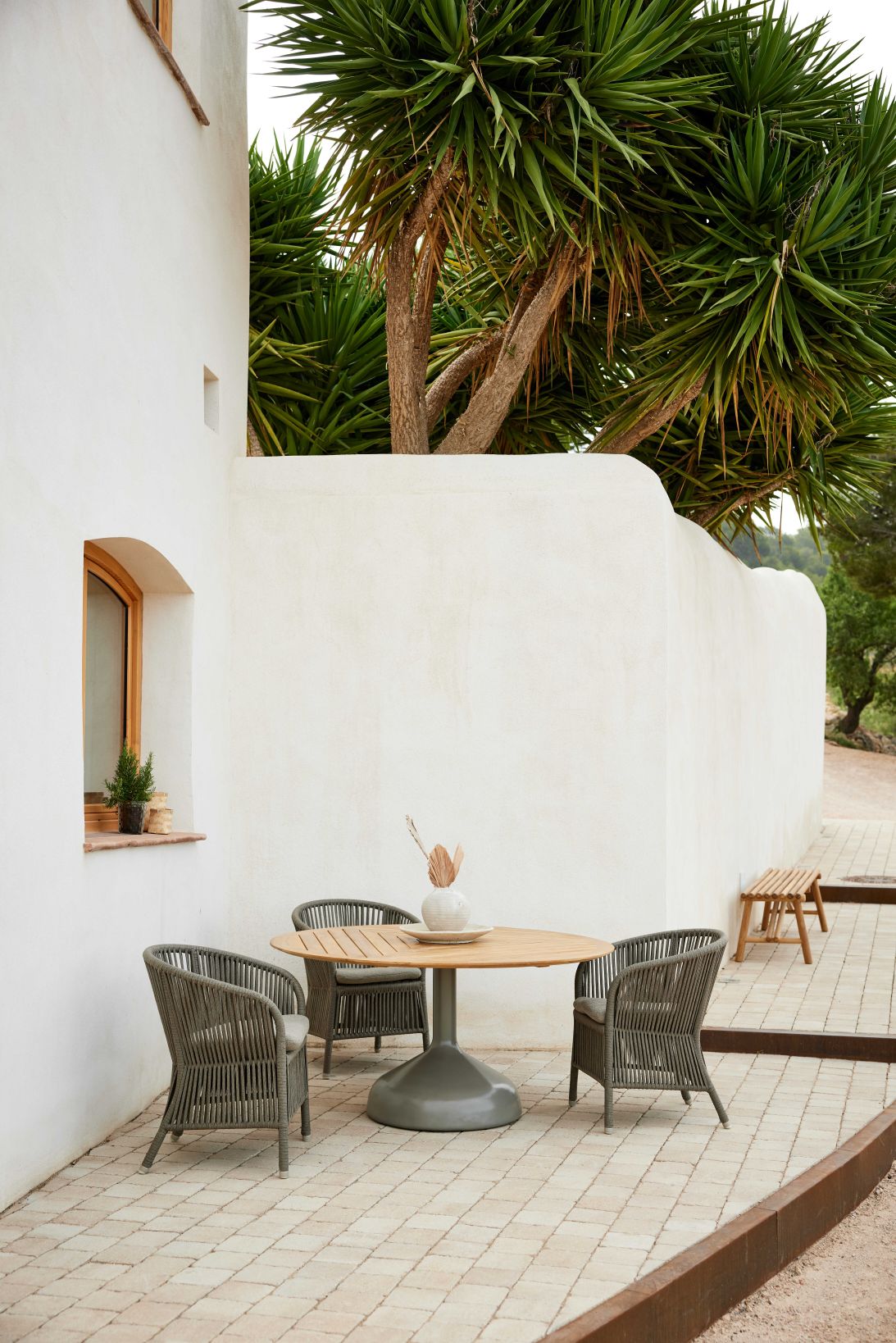 Derby Outdoor Sessel von Cane-Line in Taupe mit Tisch auf einer Terrasse.