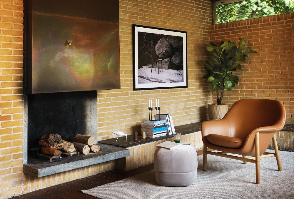 Wohnzimmer mit braunem Lounge Sessel, Ottomane und Kamin. Gemütliches Interieur mit Designmöbeln.