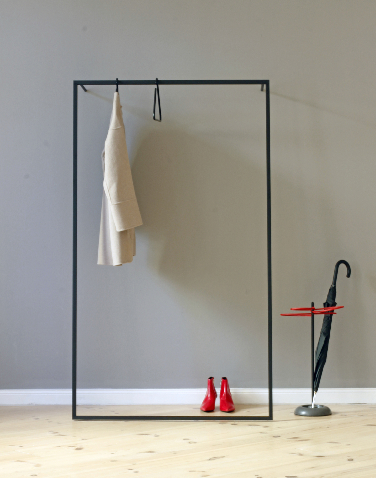 Roomsafari Leano Anlehngarderobe mit Mantel, roten Schuhen und Schirmständer vor grauer Wand. Moderne Garderobenlösung.