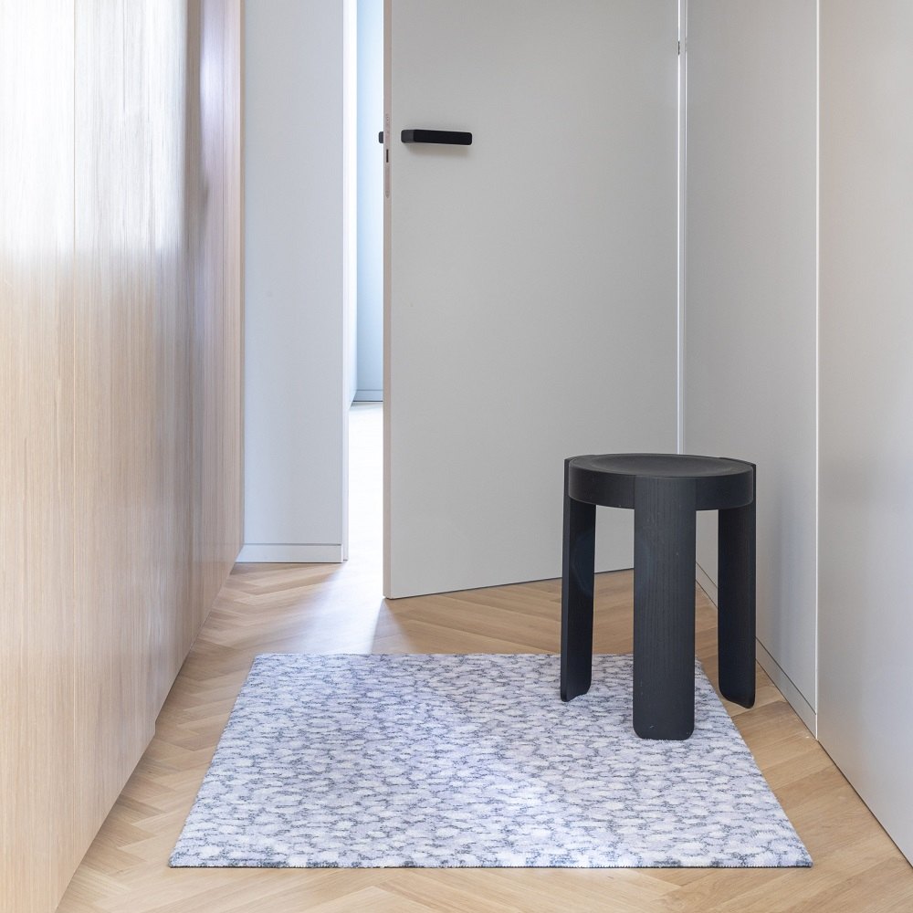Grain Amethyst Heymat Fußmatte 85x115 cm im Flur, neben einem schwarzen Hocker. Indoor Fußmatte.
