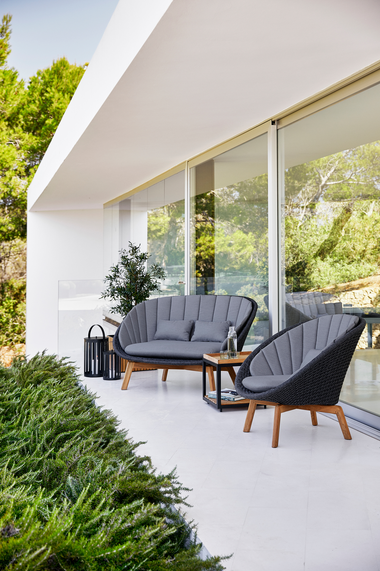 Cane-Line Peacock Outdoor Lounge Set: 2-Sitzer Sofa und Sessel auf einer Terrasse. Graue Polster.