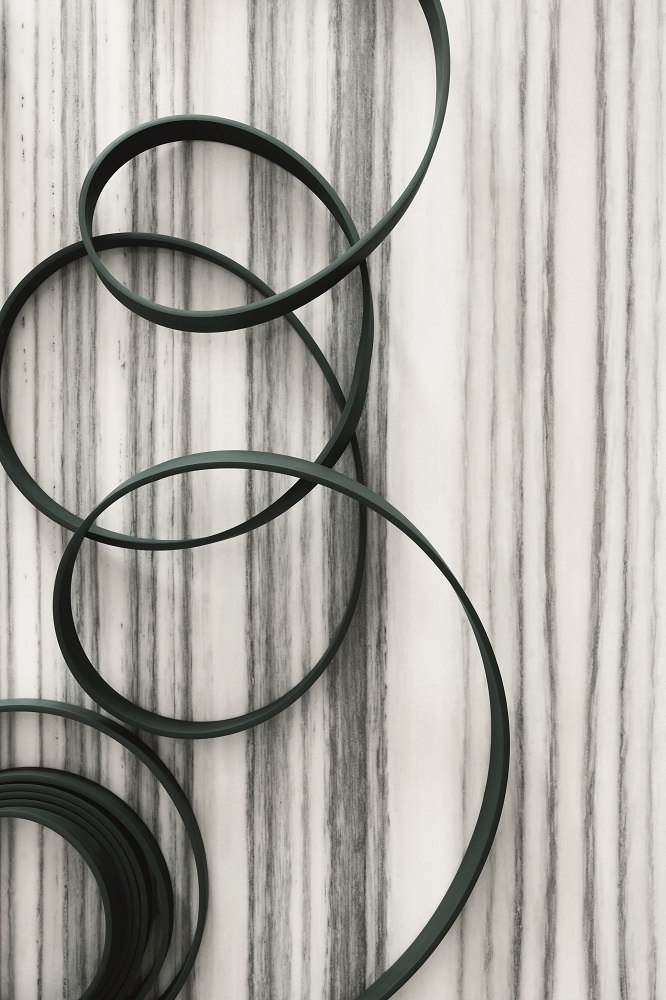 Detailaufnahme der grünen Wireline Pendelleuchte von Flos, moderne Hängeleuchte mit kreisförmigen Elementen vor Marmorwand.