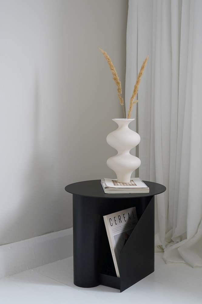 Schwarzer Sentrum Beistelltisch von Woud mit Magazinhalter, Vase und Dekoration im minimalistischen Wohnzimmer.