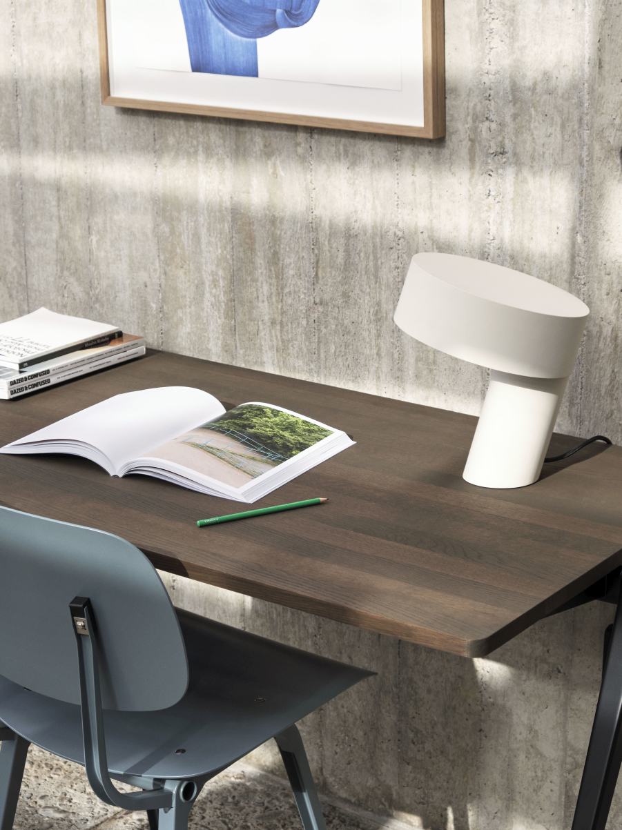 Weiße Slant Table Lamp von Hay auf einem Schreibtisch mit Buch und Bleistift.