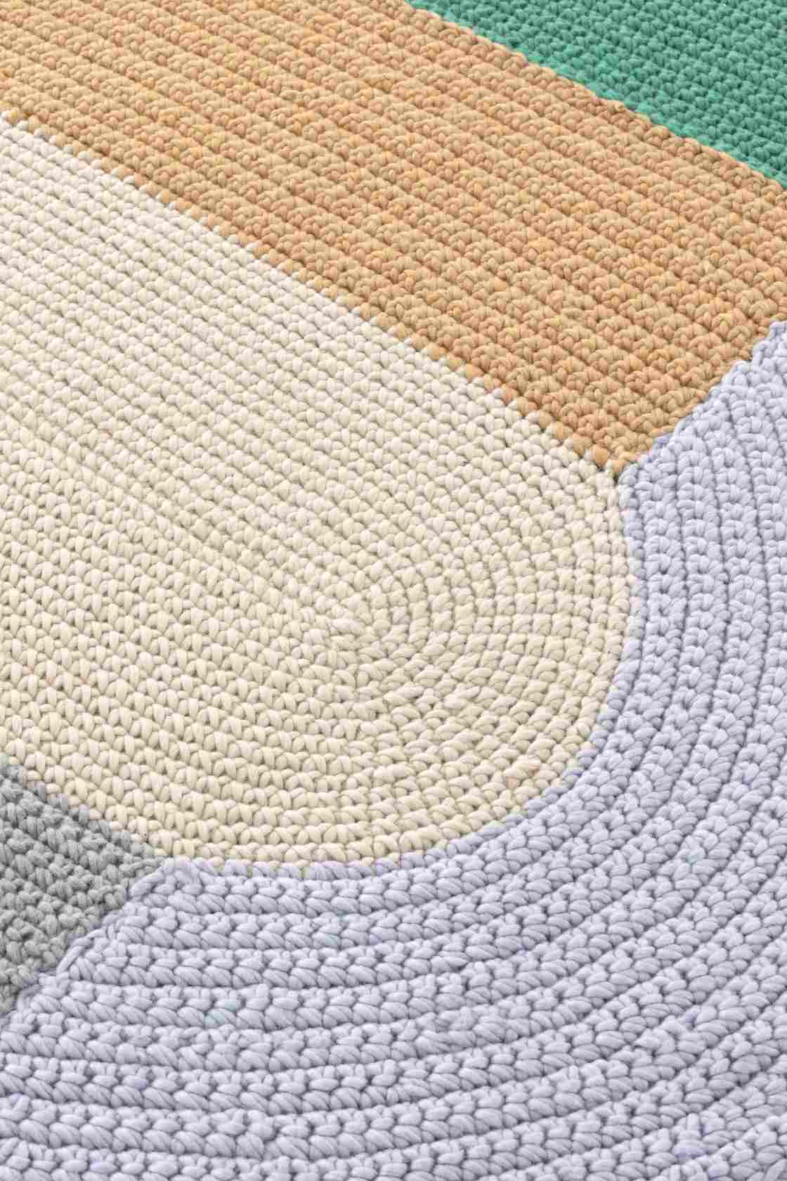 Detailaufnahme des gehäkelten Teppichs "The Crochet Collection" in Grün, Beige, Grau und Weiß.