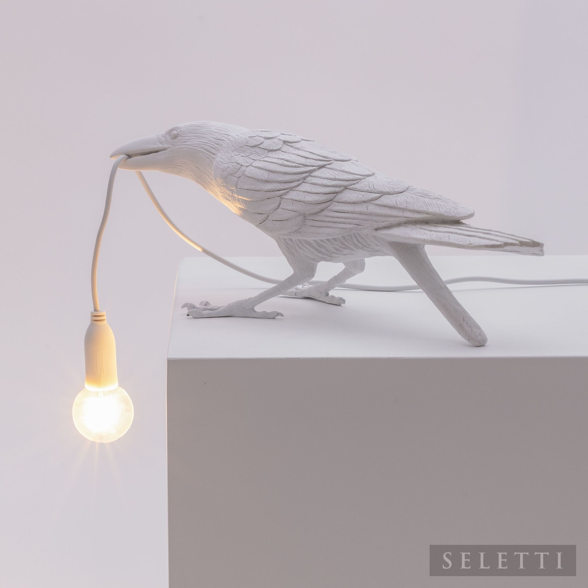 Weiße Seletti Bird Lamp "Playing" als Designleuchte, Vogel hält Glühbirne im Schnabel.