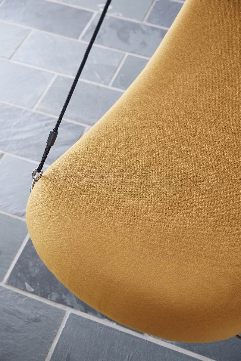 Detailaufnahme: Gelber Flying Chair Schaukelsessel mit schwarzer Aufhängung und grauem Steinboden.