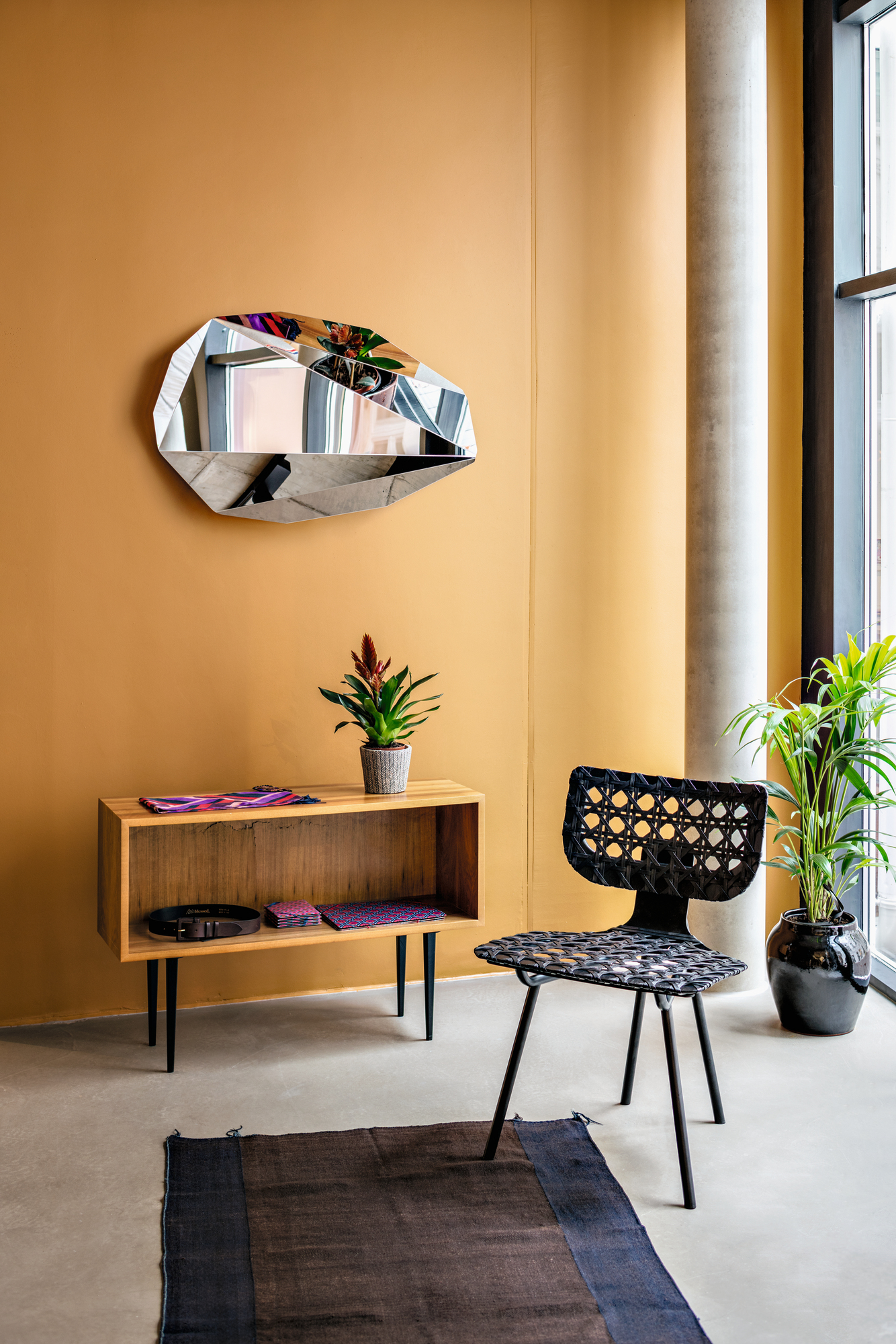 Wohnraum mit Piega Mirror Wandspiegel von Classicon, Sideboard, Stuhl und Zimmerpflanzen.