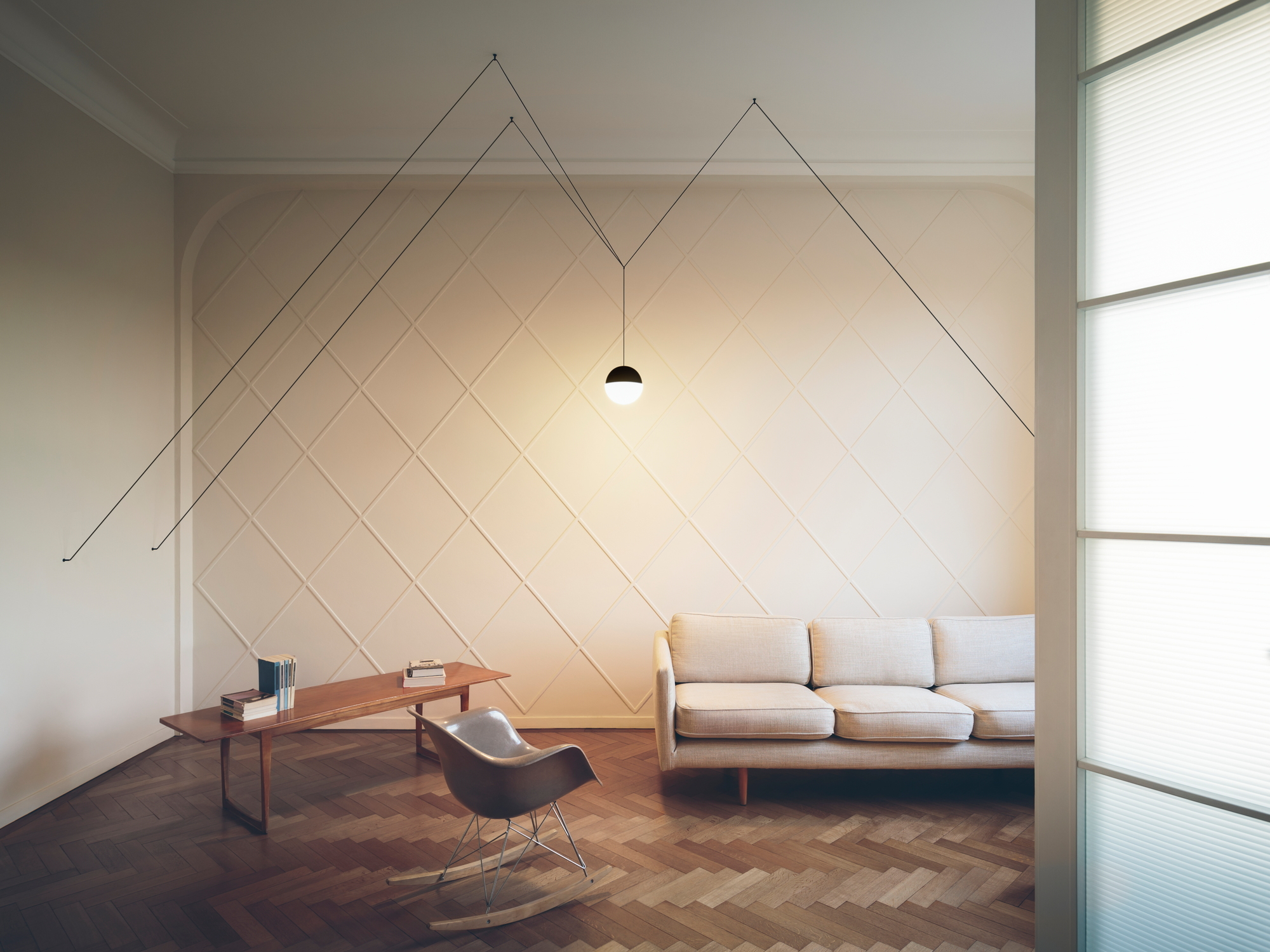 Wohnzimmer mit String Light Kugelkopf Pendelleuchte von Flos, minimalistisches Design mit Kabeln und hellem Licht.