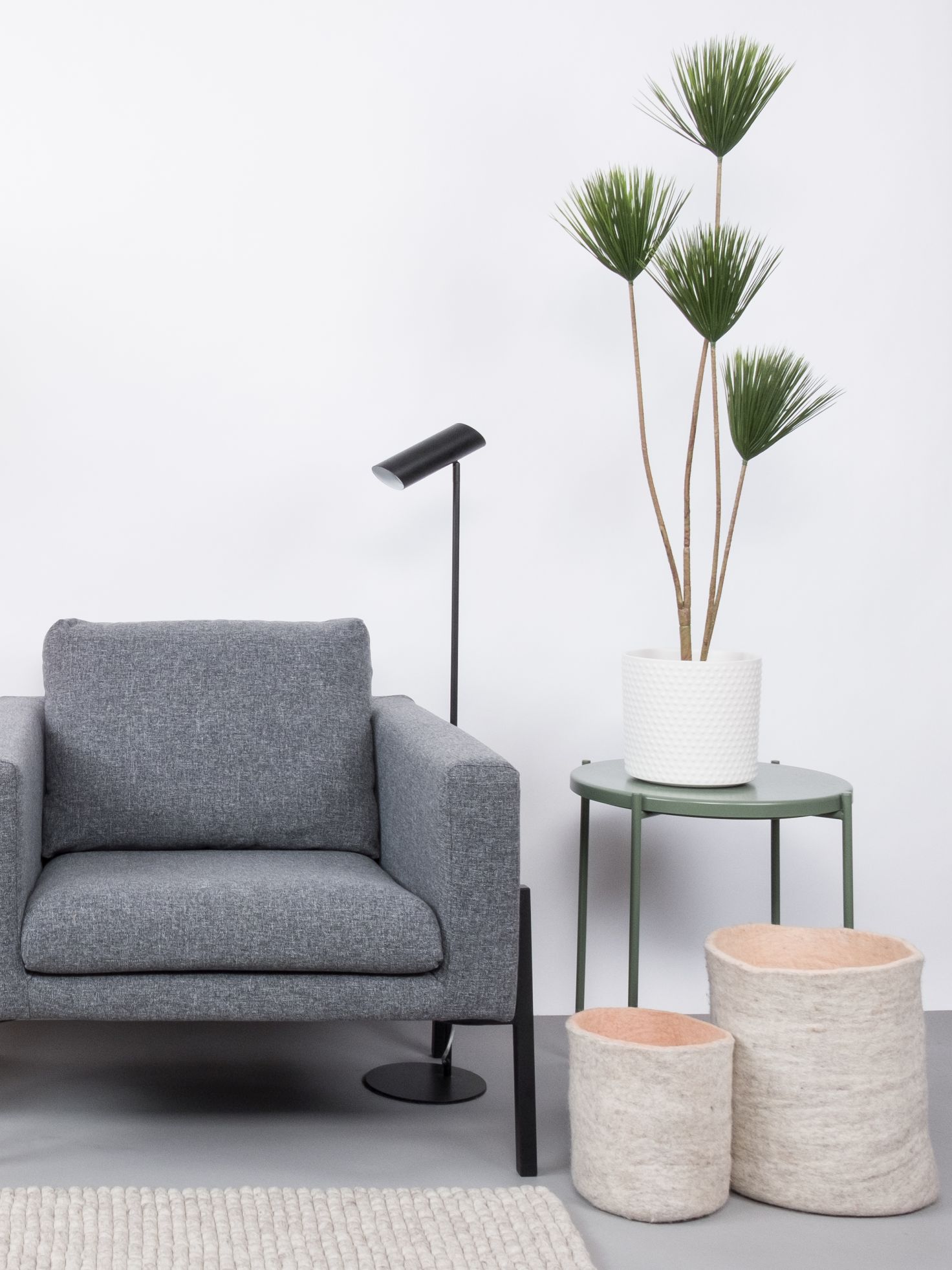Grauer Sessel mit Lampe, Beistelltisch mit Pflanze und zwei Filzkörben für modernes Wohnzimmer.