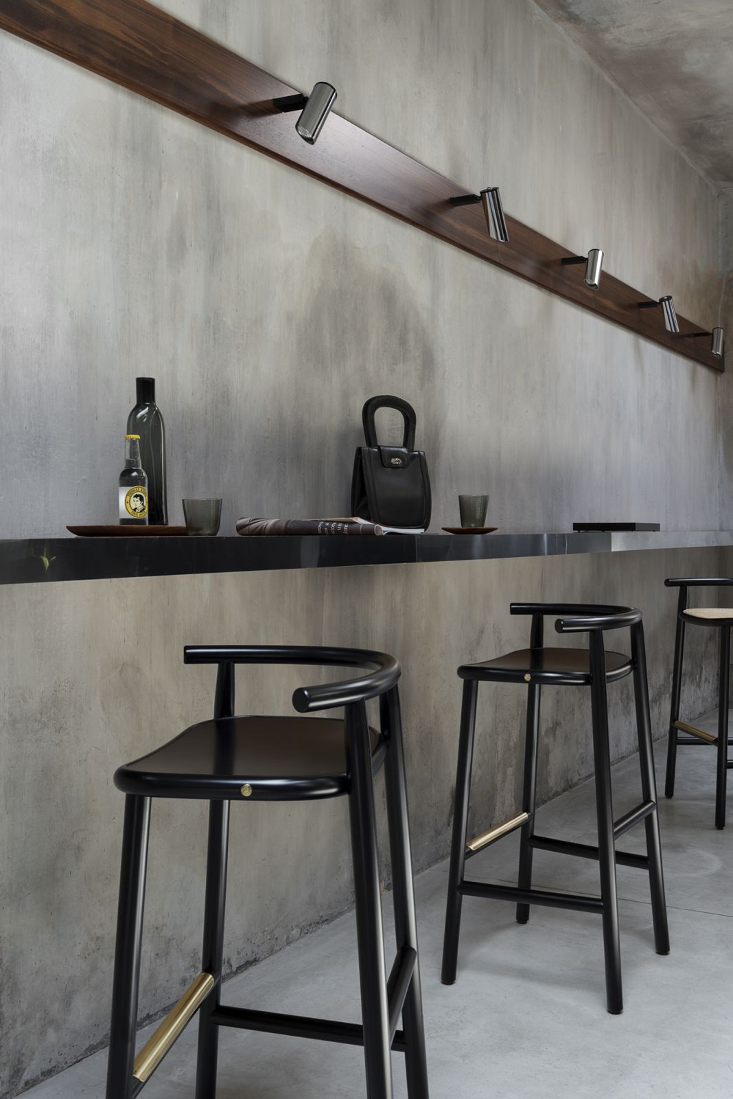 Schwarzer Single Curve Barhocker von Wiener GTV Design mit Schichtholzsitz vor grauer Wand.