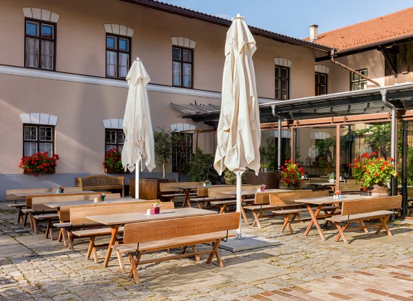Weishäupl Sonnenschirme: Außenbereich eines Restaurants mit Holztischen, Bänken und weißen, geschlossenen Teleskopschirmen für Sonnenschutz.