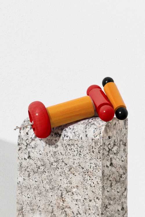 Alessi Korkenzieher ES17 mit Holzgriff in Rot und Gelb auf einem Steinsockel.