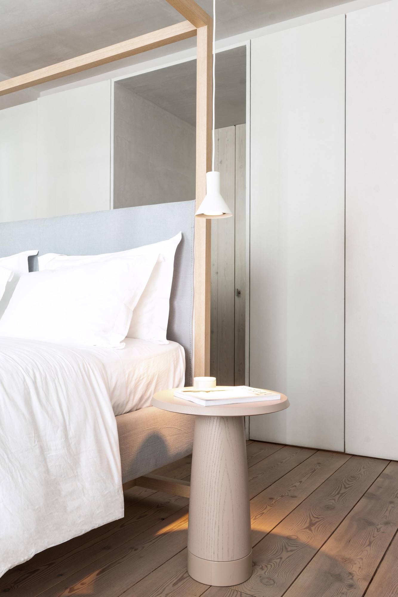Amanita Beistelltisch von Schönbuch, helles Holz, runde Tischplatte, neben einem Bett.
