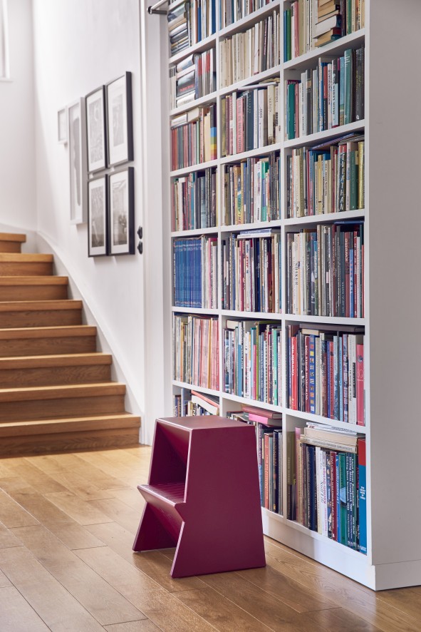 Purpurroter Mono Tritthocker von Richard Lampert vor Bücherregal und Treppe. Design Tritthocker für Wohnraum.
