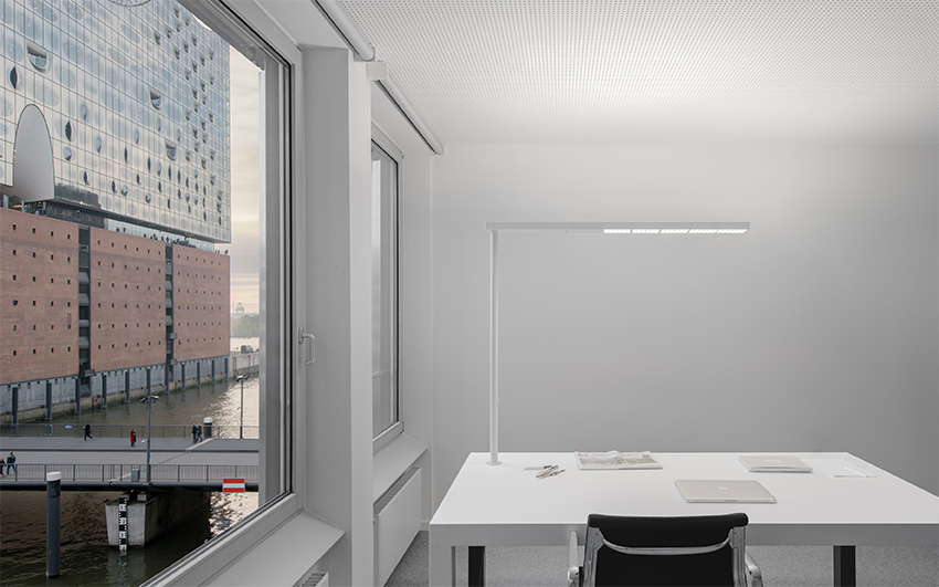 Moderne XT-A Plus Stehleuchte in Grau über einem weißen Schreibtisch mit Laptop und Büromaterial.