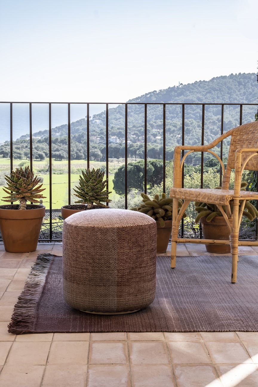 Nanimarquina Shade Outdoor Pouf Hocker auf Terrasse mit Teppich und Blick in die Natur.