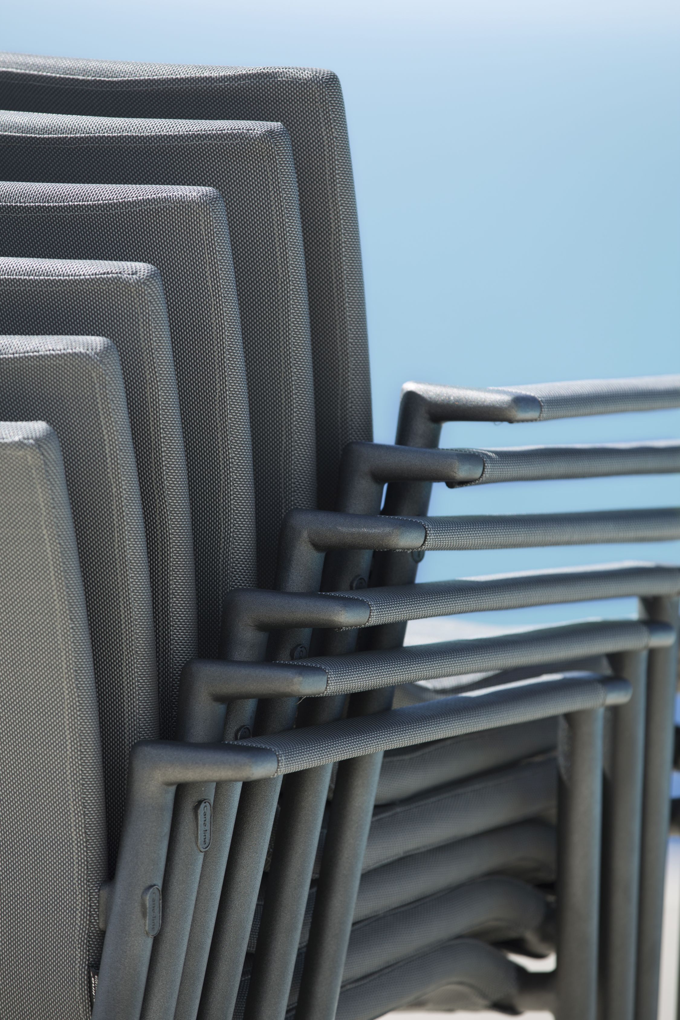 Detailaufnahme gestapelter Core Outdoor Stühle von Cane-Line in Taupe, mit Armlehnen und AirTouch-Gewebe.
