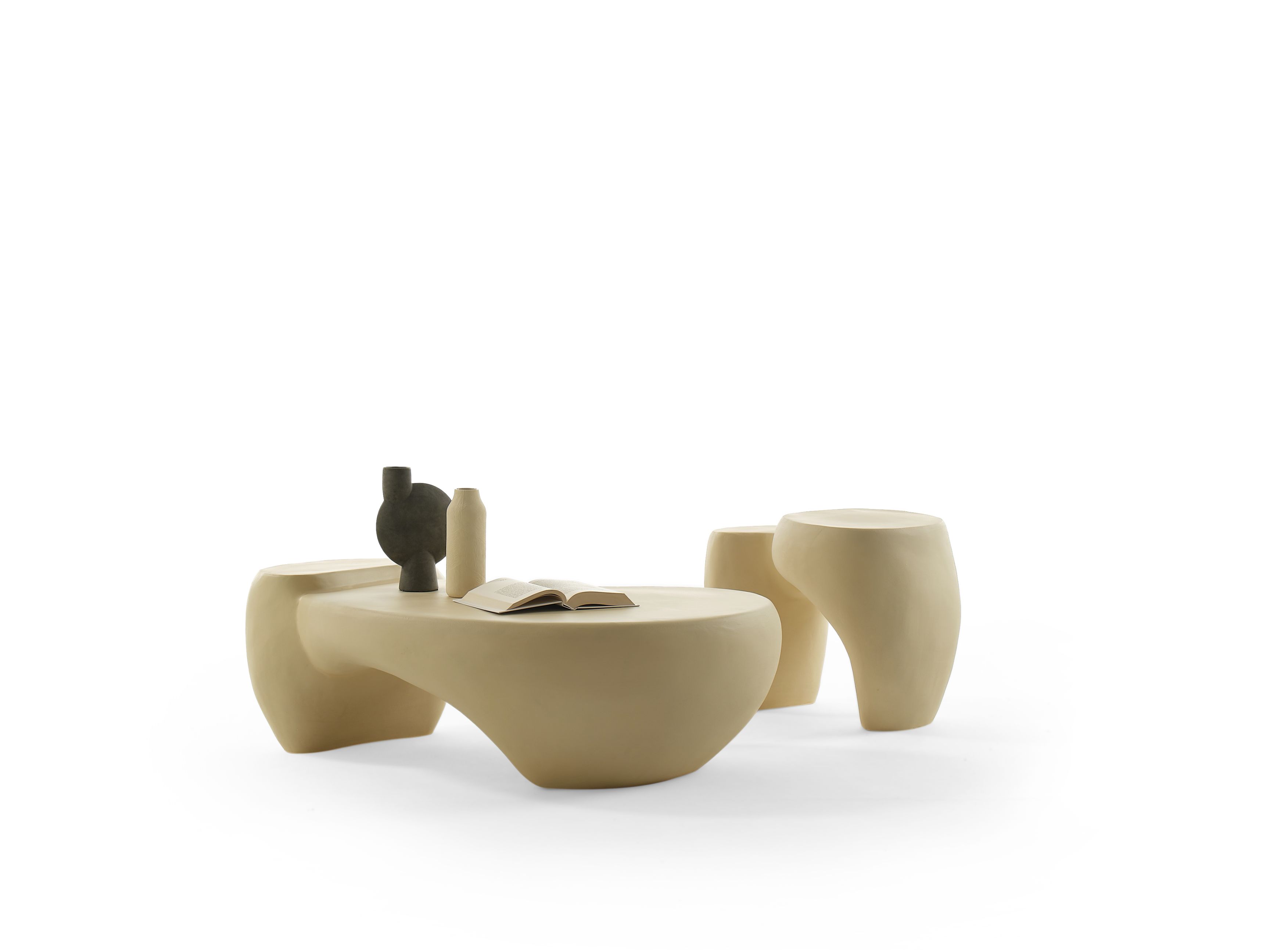 Elfenbeinfarbener Couchtisch "Dune" von Mogg mit Dekoration und zwei passenden Hockern auf weißem Hintergrund.