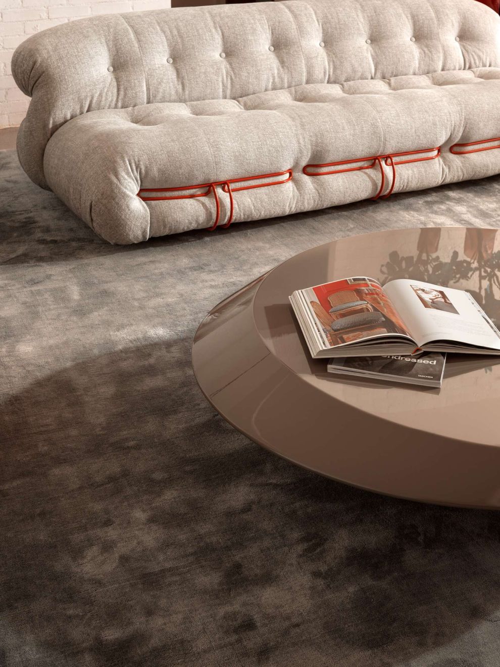 Beige Soriana Sofa mit Knopfheftung und roter Akzentuierung, kombiniert mit modernem Couchtisch und Teppich.