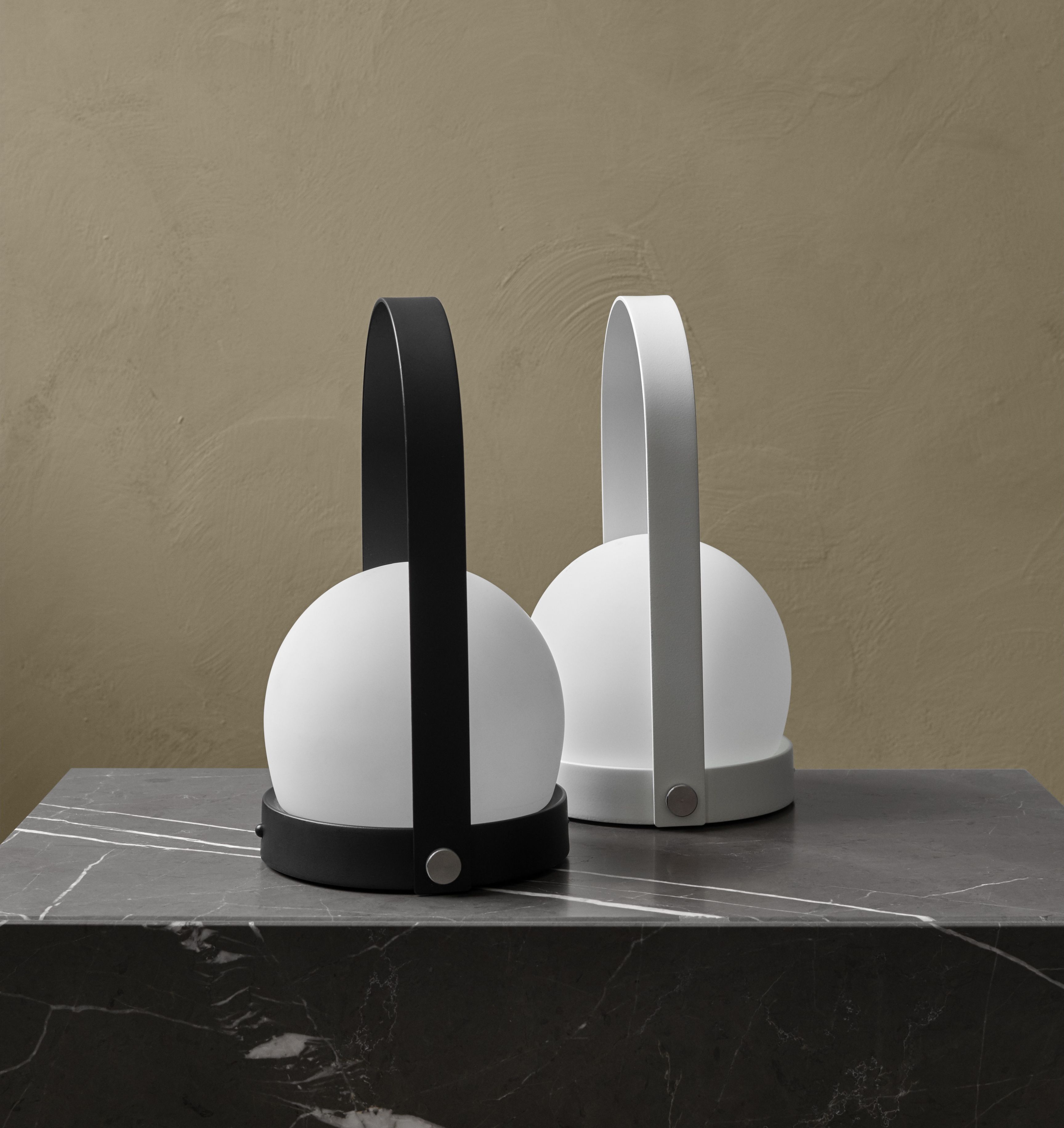 Zwei Carrie Tischleuchten: Eine schwarze und eine weiße Akkuleuchte auf einem Marmortisch.