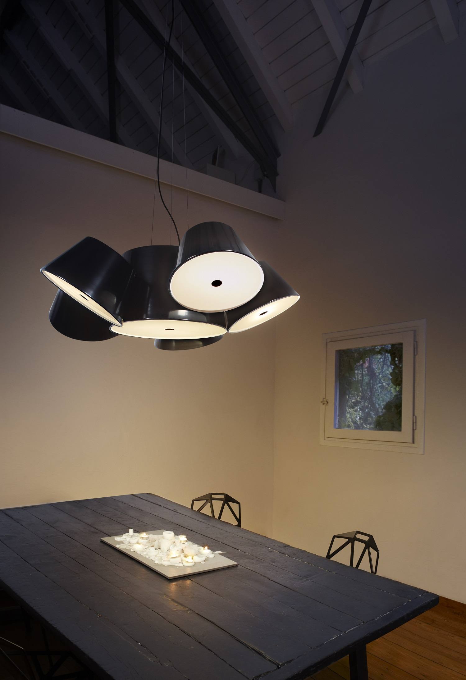 Tam Tam 5 LED Pendelleuchte von Marset über Esstisch mit Kerzen und zwei Stühlen.
