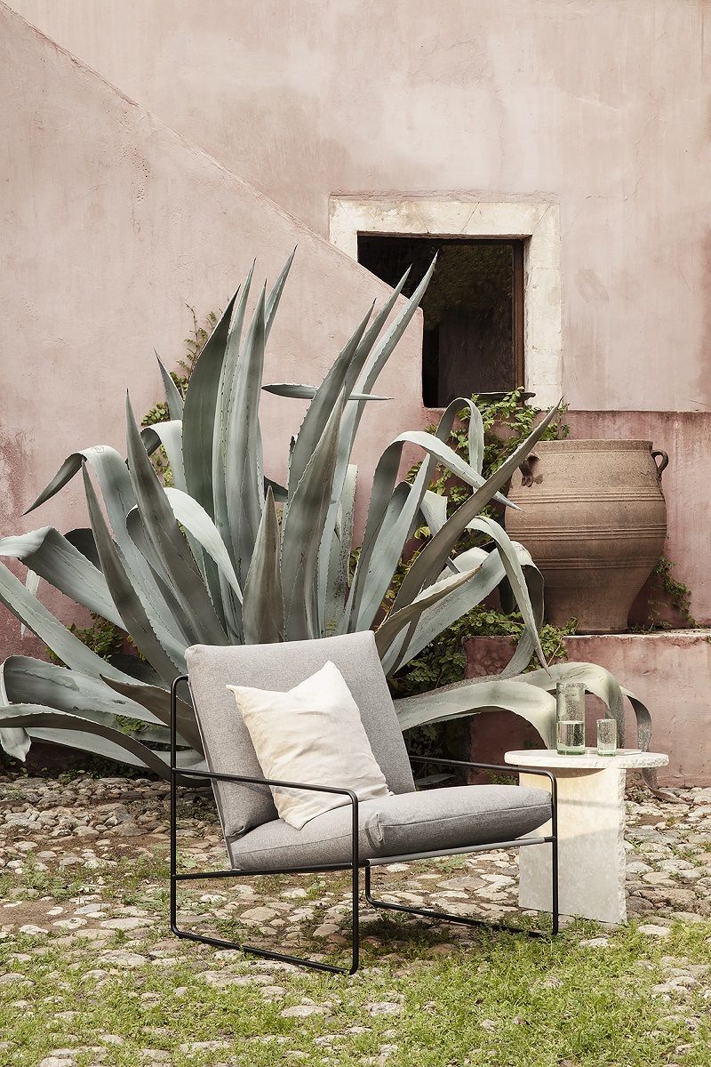 Graues Ferm Living Desert Outdoor Sofa mit Kissen und Beistelltisch im Garten.