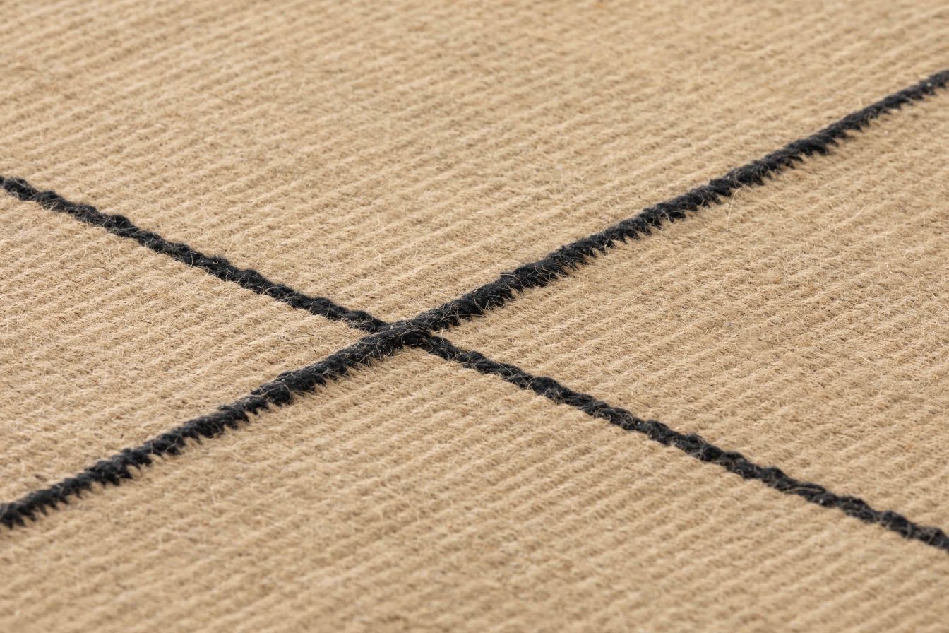 Detailansicht des Roots Teppichs von Gan, 192x240cm, mit schwarzem Kreuzmuster auf beigem Untergrund.