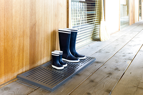 Schönbuch Drip Schuhablage Gross mit Gummistiefeln in verschiedenen Größen auf einem Holzboden.