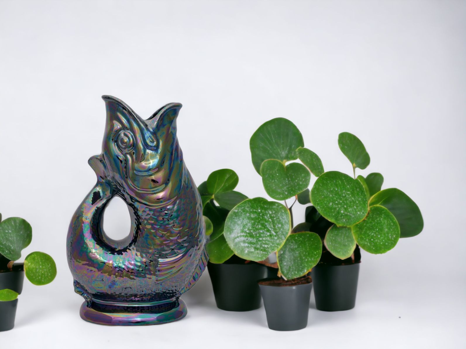 Gluckigluck Fisch Karaffe in irisierendem Lustre-Finish, neben kleinen Zimmerpflanzen auf weißem Hintergrund.