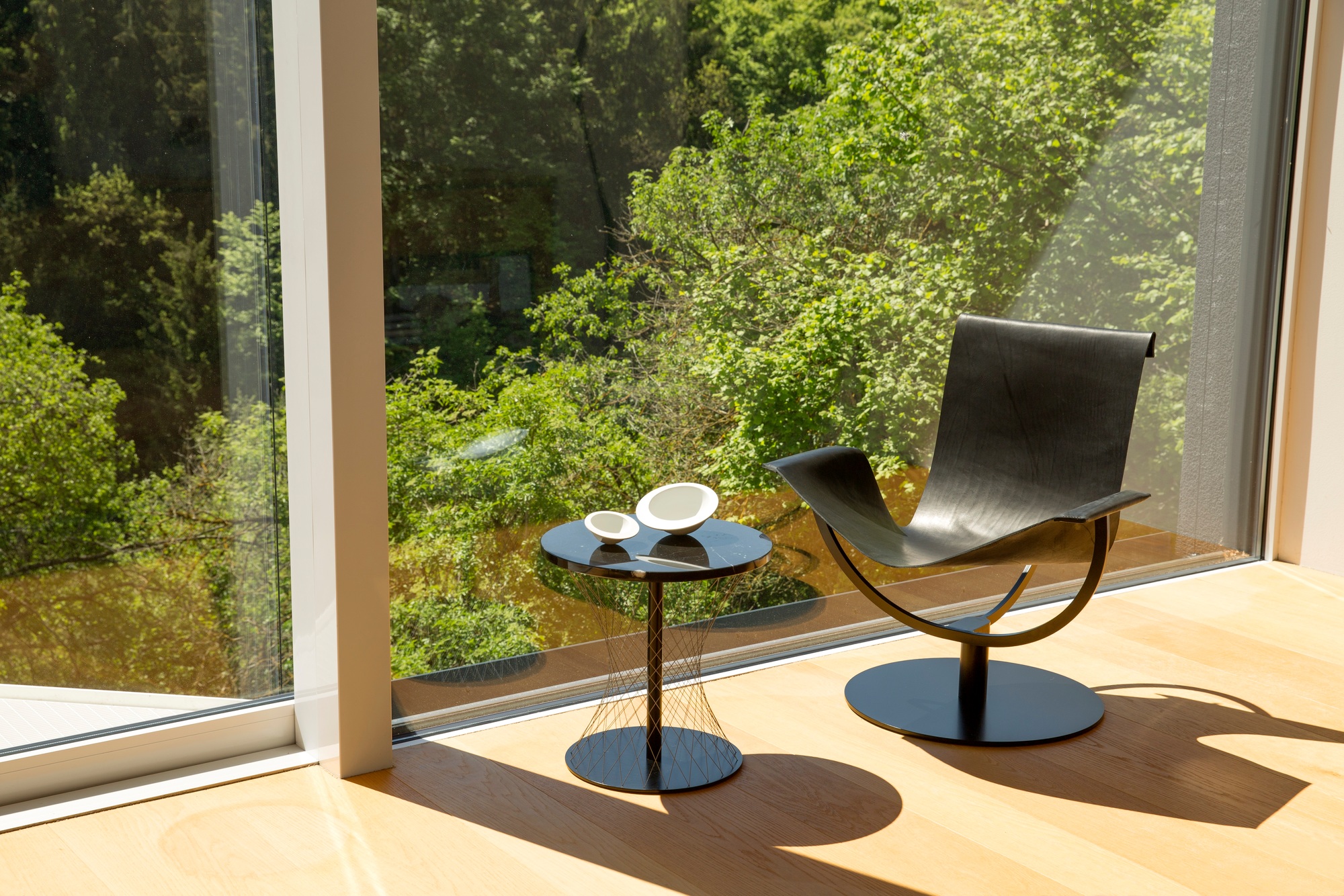 Schwarzer Network Beistelltisch Favius neben Sessel vor Fenster mit Blick ins Grüne. Moderner Beistelltisch.