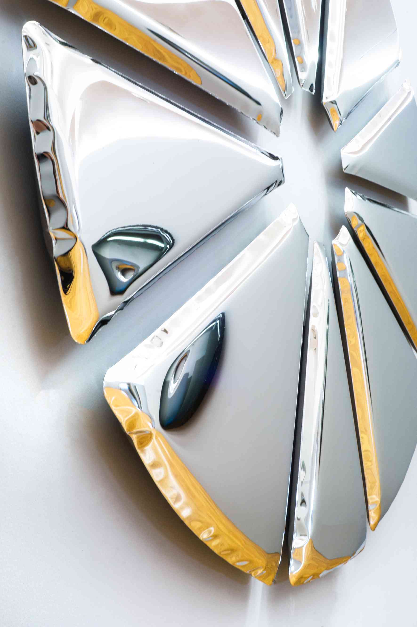 Nahaufnahme des Nucleus Spiegel Zieta, ein moderner Wandspiegel mit silbernen, dreieckigen Elementen und goldenen Akzenten.