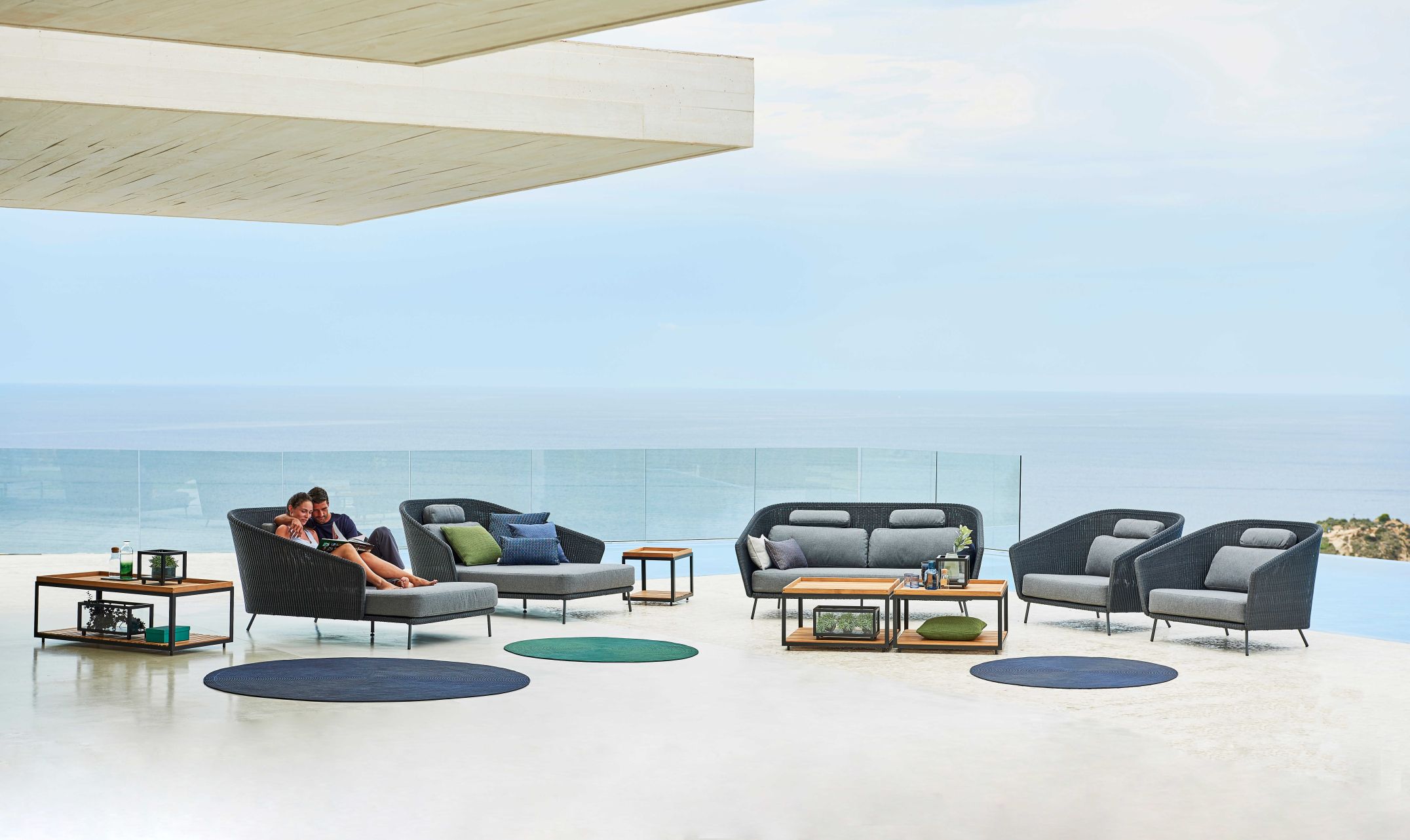 Cane-Line Mega Outdoor Daybed mit Rattan-Optik und grauen Polstern, Teil einer Lounge-Gruppe im Freien.