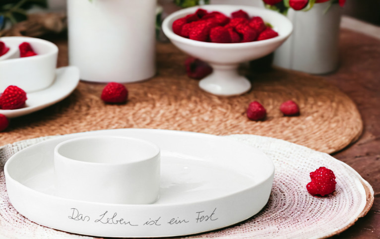 Weiße Räder Schale "Das Leben ist ein Fest" mit Dipschale und Himbeeren als Tischdeko.
