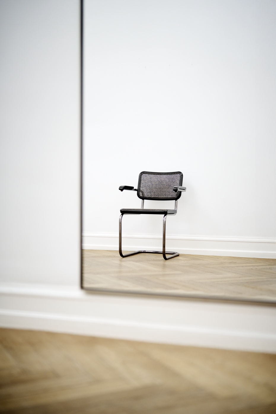 JS. Thonet S 64 V Freischwinger Stuhl mit Armlehnen und Rohrgeflecht vor weißer Wand.