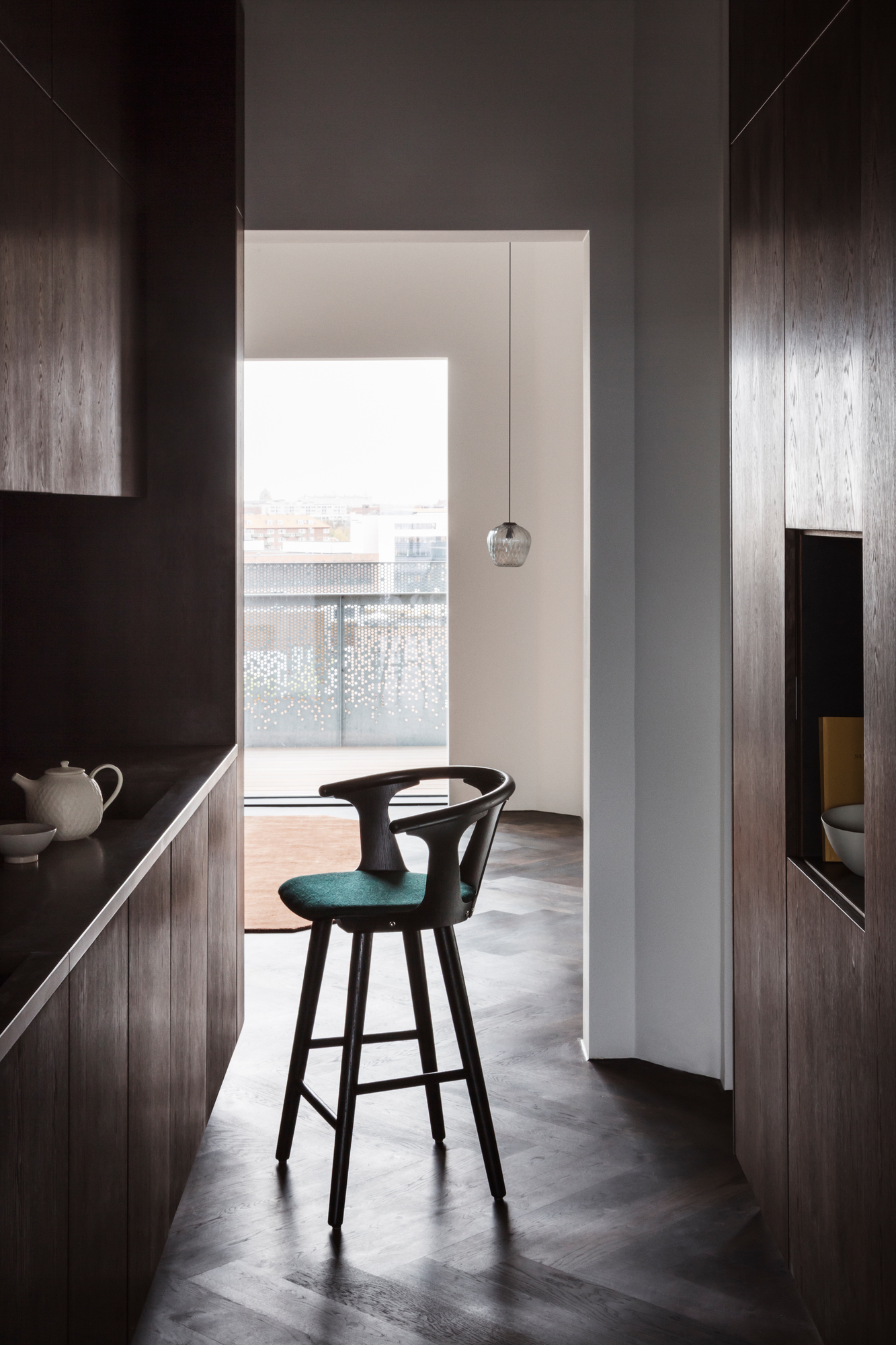 AndTradition Blown Pendelleuchte über Barhocker in moderner Küche mit dunklen Holzschränken und Parkettboden.