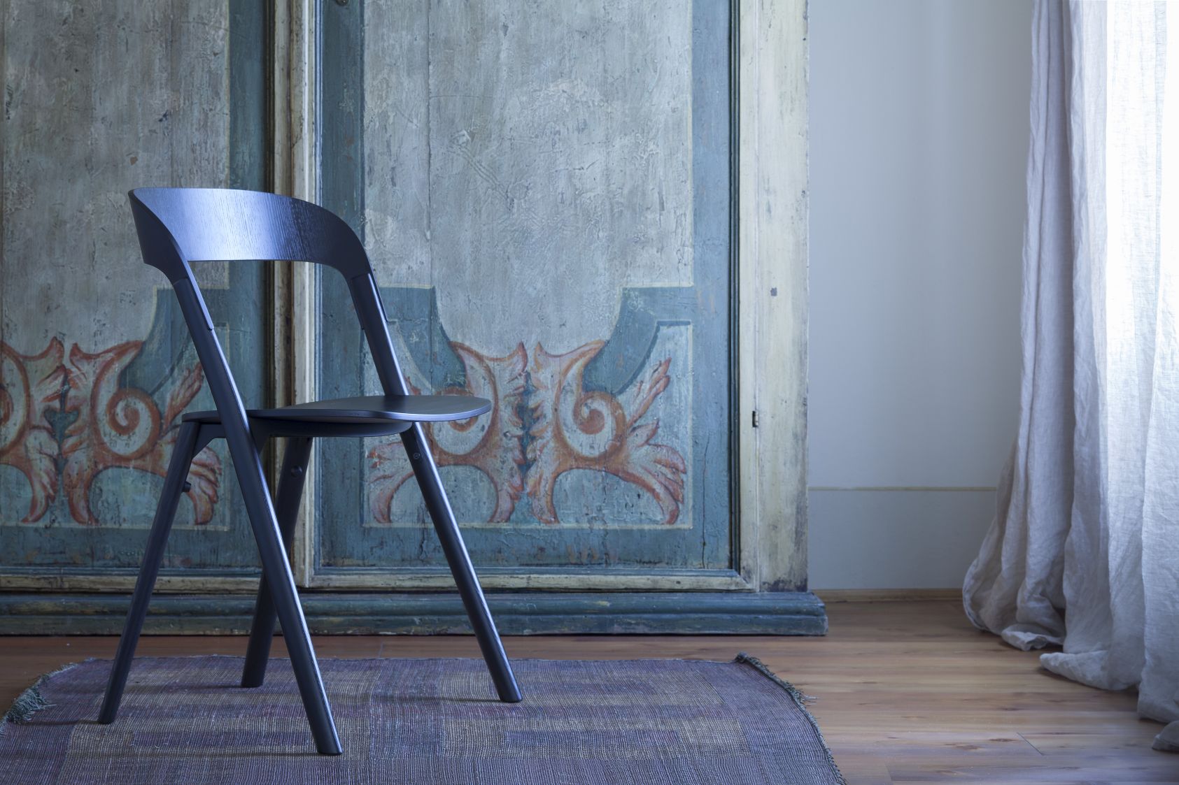 Pila Stuhl von Magis, ein moderner Holzstuhl in dunkler Farbe vor antikem Schrank.