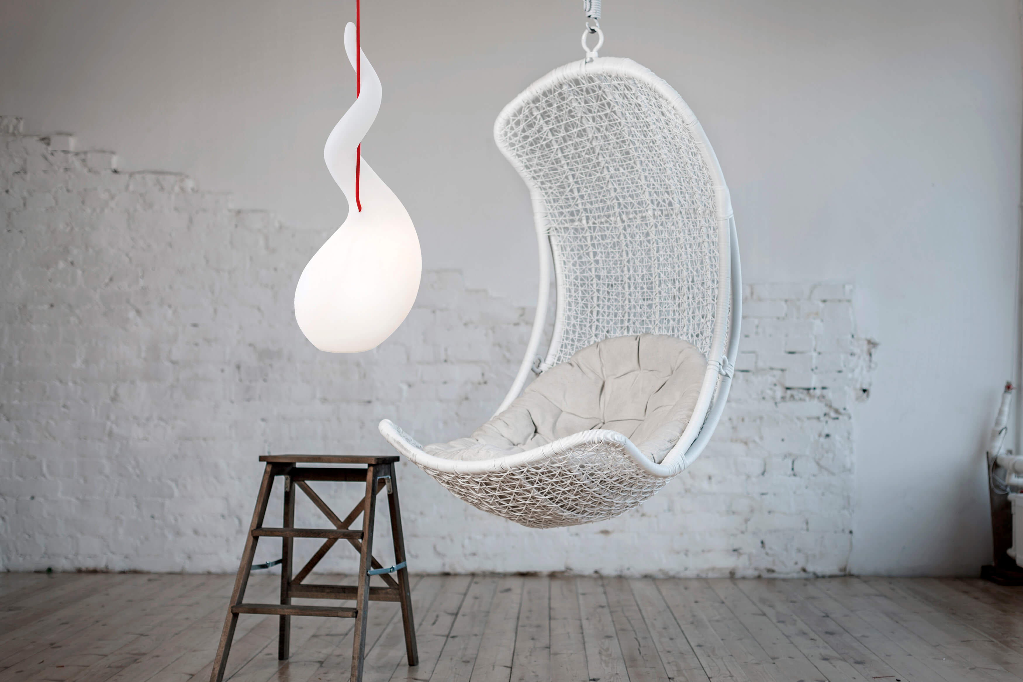 Alien PL Pendelleuchte: Moderne Hängeleuchte in Tropfenform mit roter Zuleitung, neben einem Hängesessel.