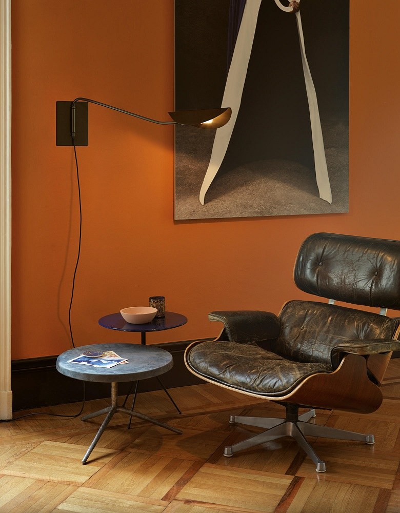 Nahaufnahme der Oluce Plume Wandleuchte in einem Wohnzimmer mit Sessel und Beistelltischen.