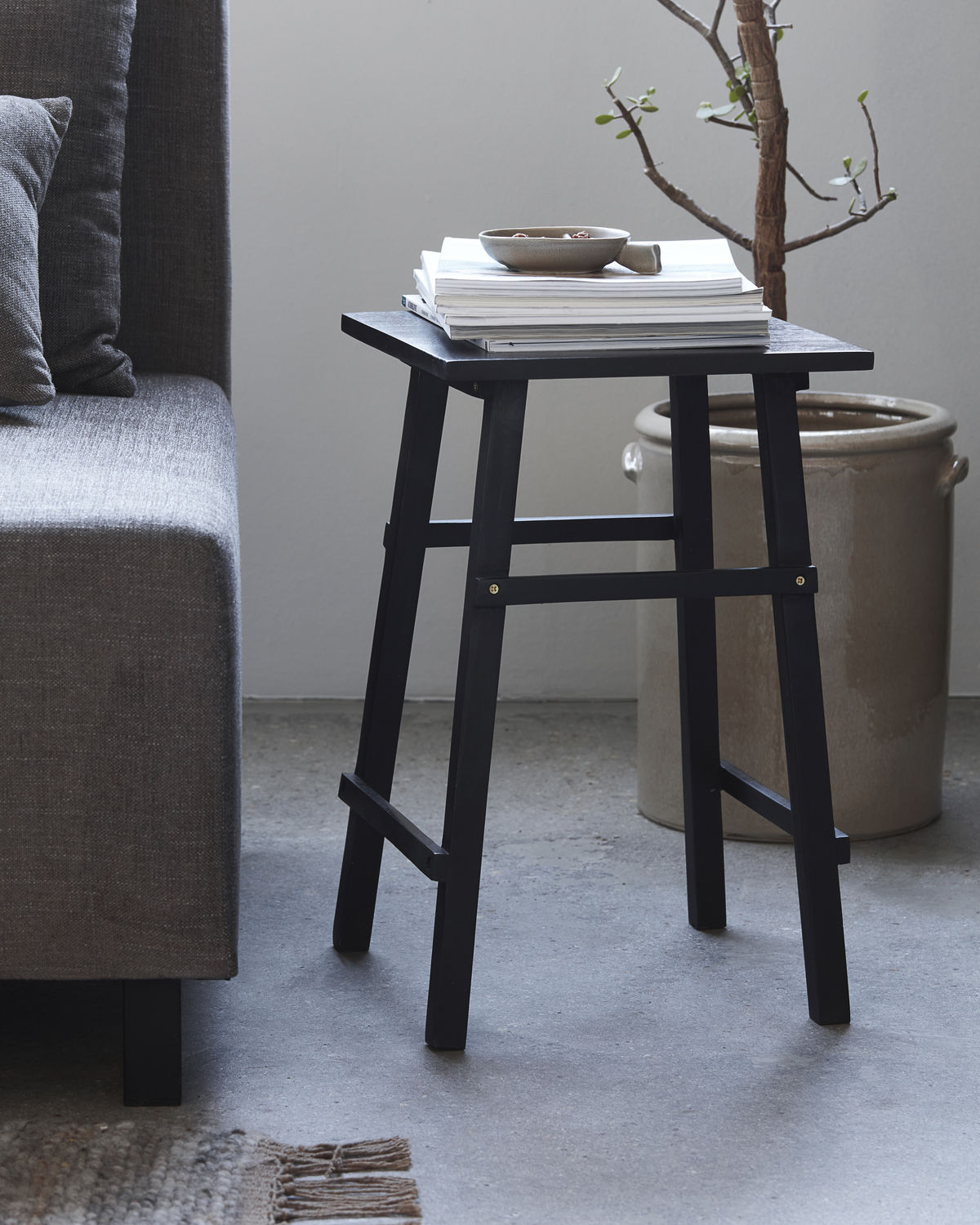 Schwarzer Laddi Beistelltisch von House Doctor neben einem Sofa, dekoriert mit Büchern und einer Schale.