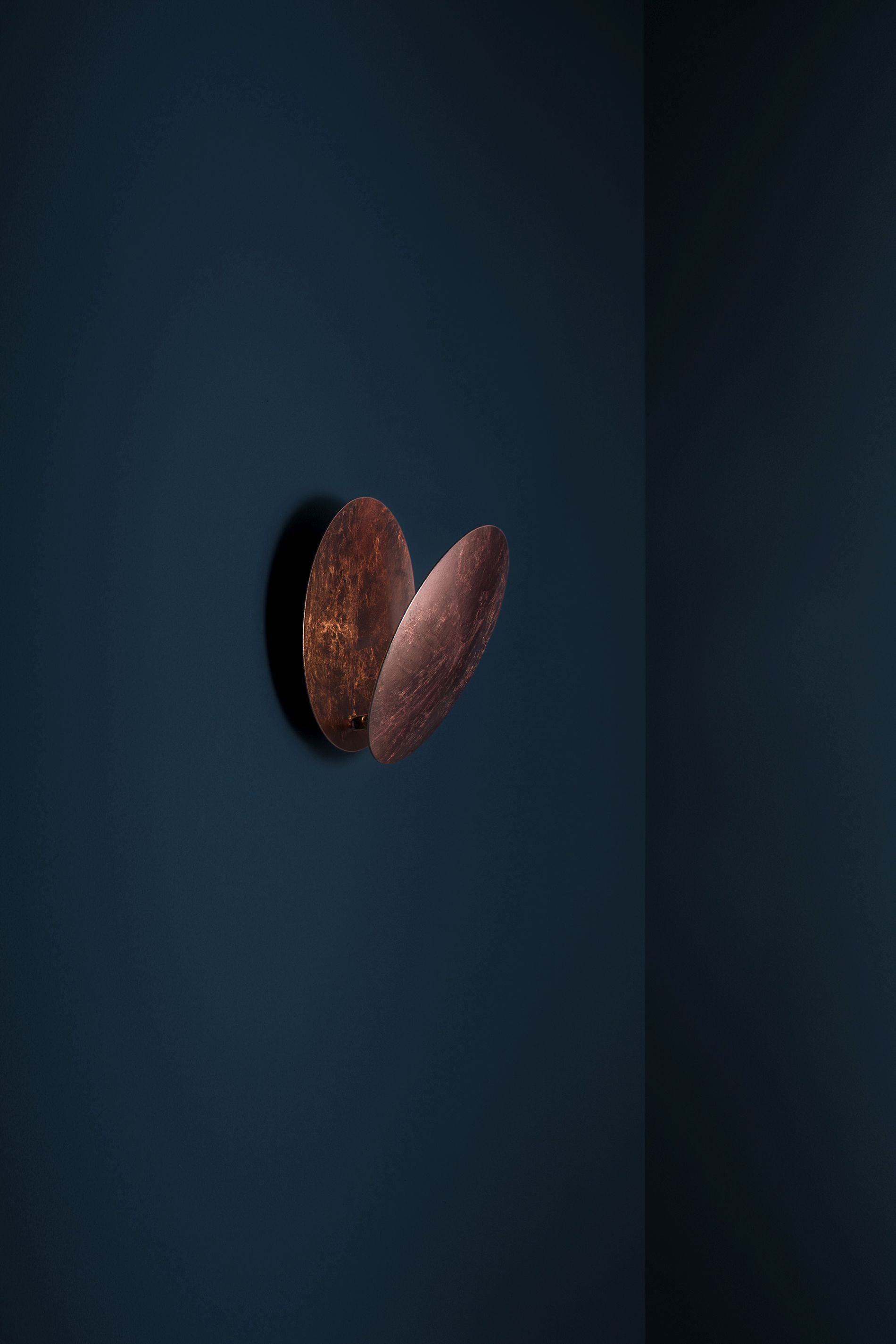 Lederam Wandleuchte von Catellani & Smith in Kupferoptik an dunkler Wand. Designleuchte für Wohnräume.