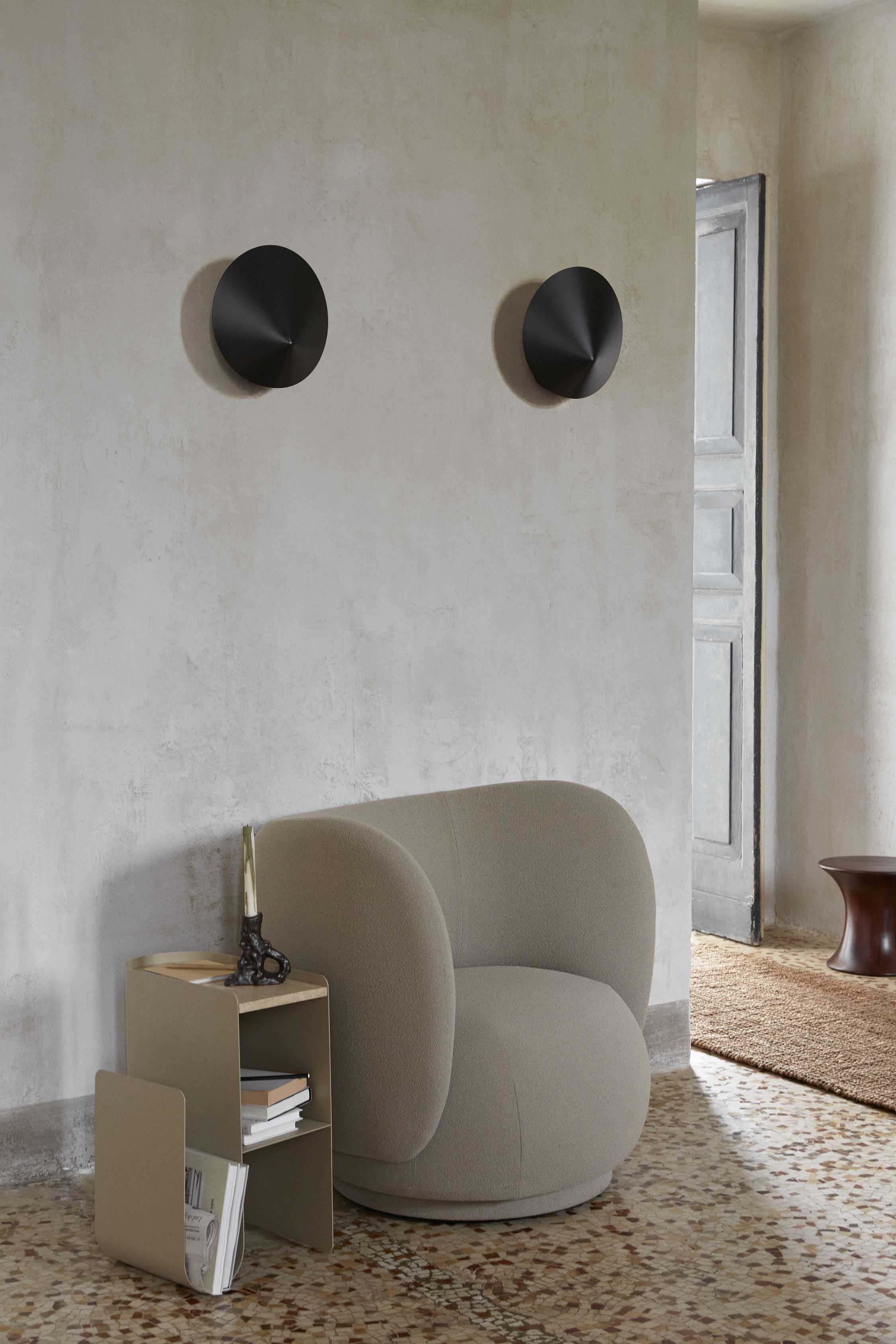 Zwei schwarze Arum Wandleuchten von Ferm Living über einem Sessel und einem Beistelltisch.