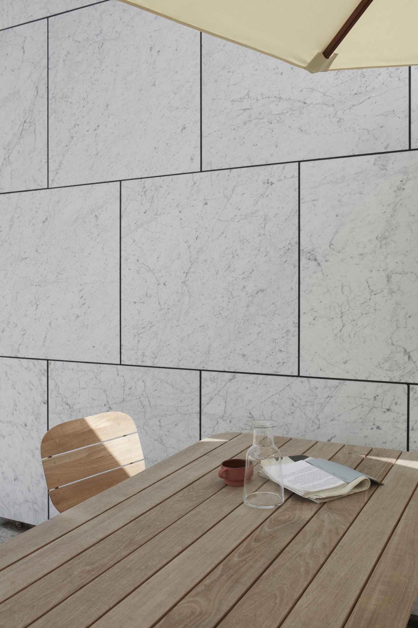 Lilium Chair Outdoor Stuhl von Skagerak: Holzstuhl am Tisch mit Getränken und Zeitung.